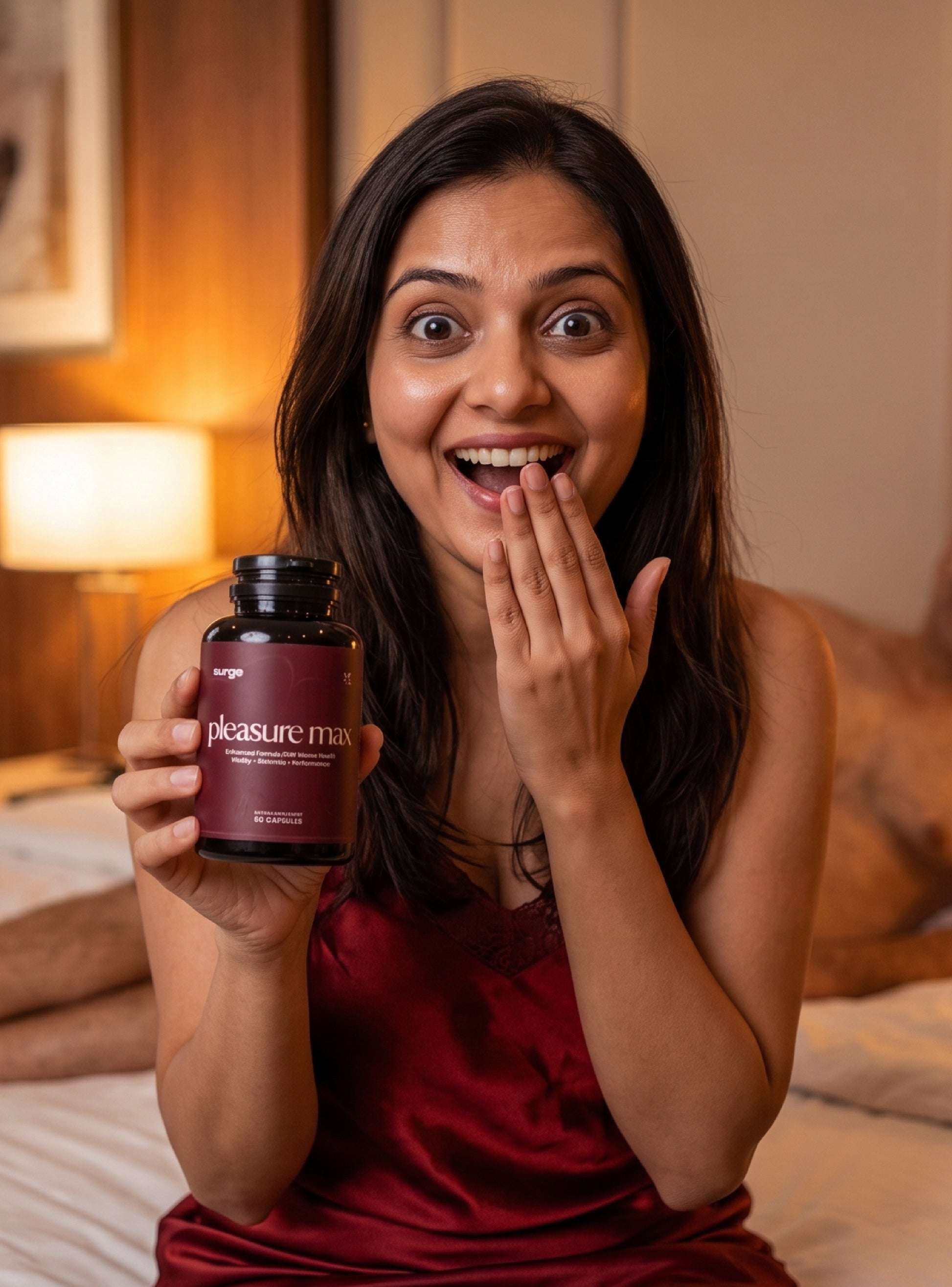 A woman in a red satin robe sits on a bed holding a bottle of 'pleasure max' supplements, with a surprised and happy expression.